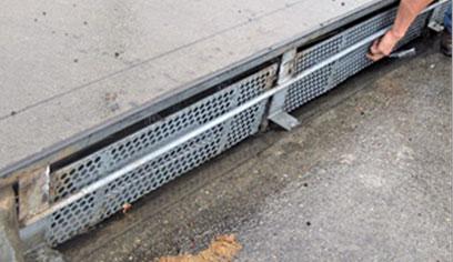 Automatic curb inlet cover: curbside water inlet with metal plate that has one inch holes for water to pass through. The metal plate has a horizontal bar running through the center that pivots the screen to close when trash pushes up against the grate.