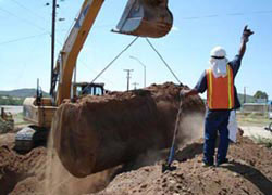 A dirt covered Underground Storage Tank being lifted from the ground by an excavator