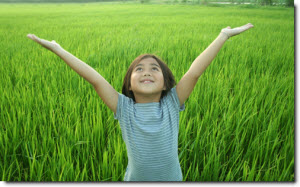 girl standing in green grass, smiling while looking up and raising her arms
