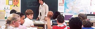 Teacher in front of class and child with hand raised.