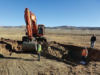 Image of earthmover removing topsoil in an arid grassland with lower hills in distance.