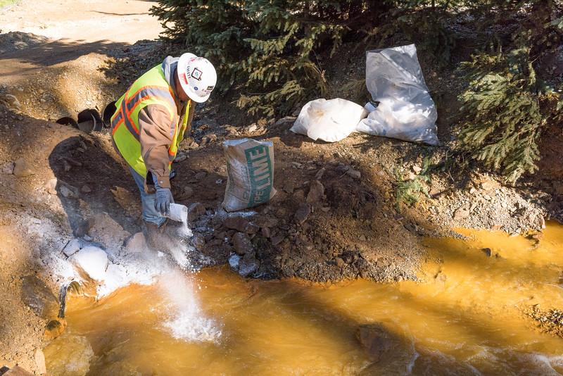 a man in a hard hat sprinkling lime (white power) into a pool of muddy water next to a culvert