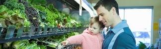 Image of a man holding a little girl who is pointing to produce in the grocery store