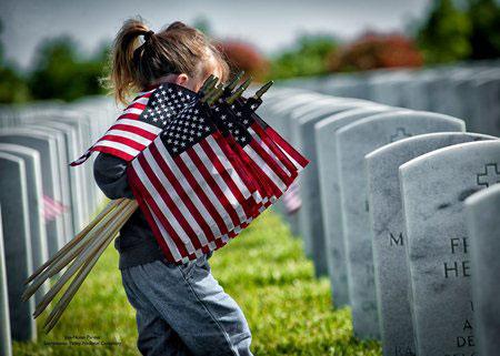 Girl carrying U.S. flags walking between tombstones