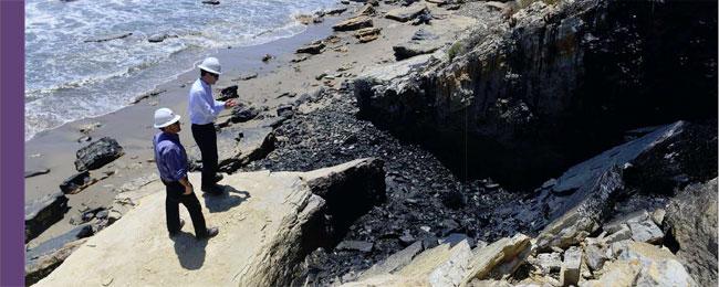 EPA Inspectors wearing safety gear standing on rocks near the ocean.