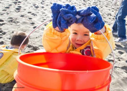 Photo of kid with bucket cleaning up at the beach