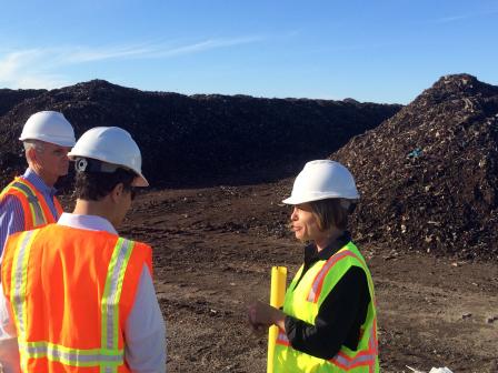 Greenwaste Director Emily Hanson talking with two others, all wearing hard hats and safety vests, in front of piles of fresh compost.