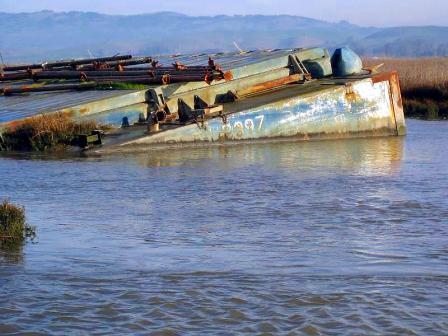 Photo of an abandoned, derelict boat that has partially sunk along a river bank