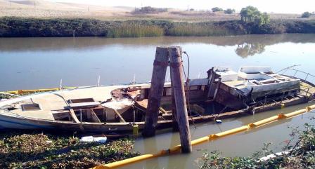 Photo of an abandoned, derelict boat that has partially sunk along a river bank