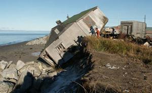 Photograph of seaside house that lies nearly on its side with one end on higher sands and one side on the beach.