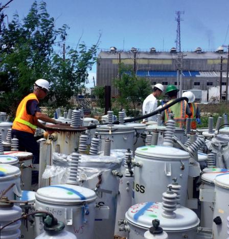 Workers inspecting a large number of power transformers near an industrial facility