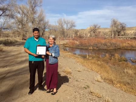 Man and woman displaying a plaque alongside a river.