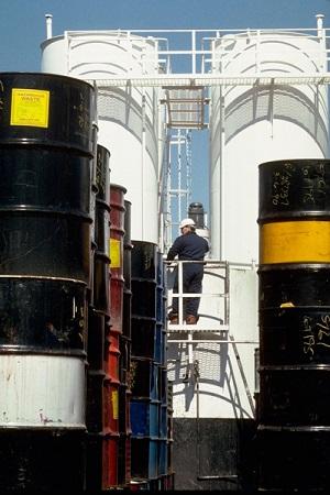 A man climbing a ladder between two large barrels of chemicals