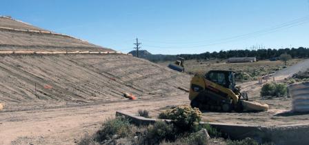 Steam roller and loader working in area of bare dirt, sloped hillside, with berms encircling