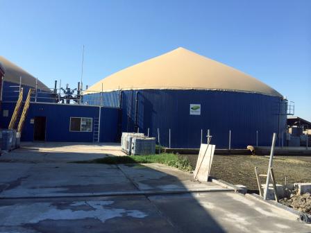 Large blue cylindrical tanks with fabric domes and connecting industrial building.