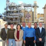 Group of people standing in front of a power plant with the Texas A&M logo.