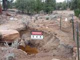 sign attached to barbed wire surrounding a hole in the ground reads: DANGER: HAZARDOUS MINE OPENING - STAY OUT & STAY ALIVE\"